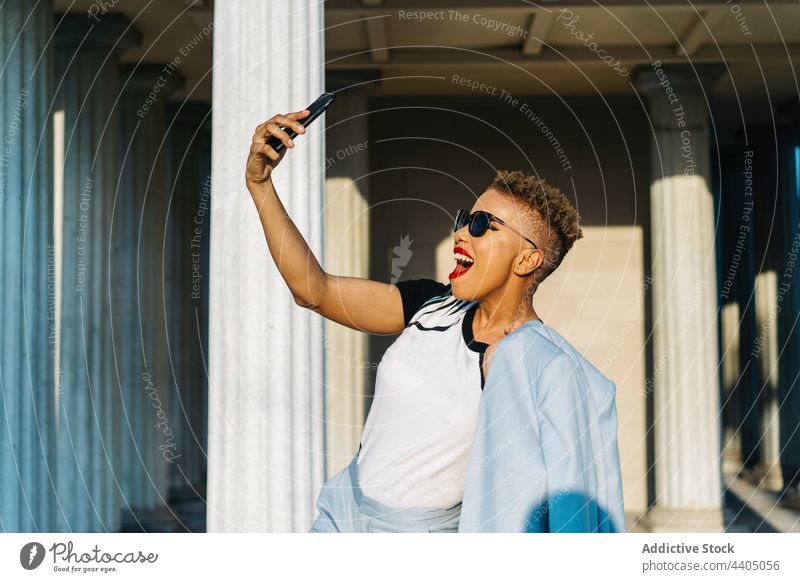 Trendy ethnic woman in sunglasses taking selfie on smartphone on street fashion style individuality cool cheerful smiling happy haircut using gadget device