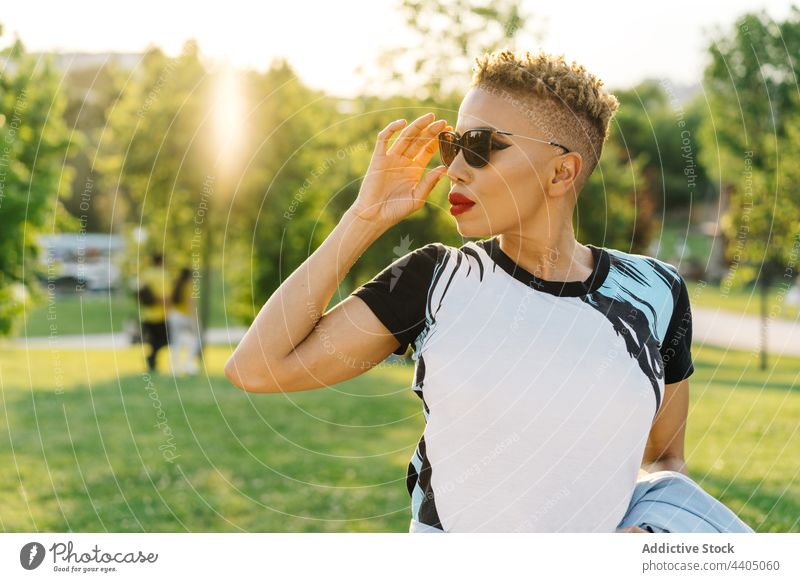 Stylish black woman in sunglasses on bench in park fashion trendy individuality cool haircut style contemplate pavement stylish tile town natural lawn tree