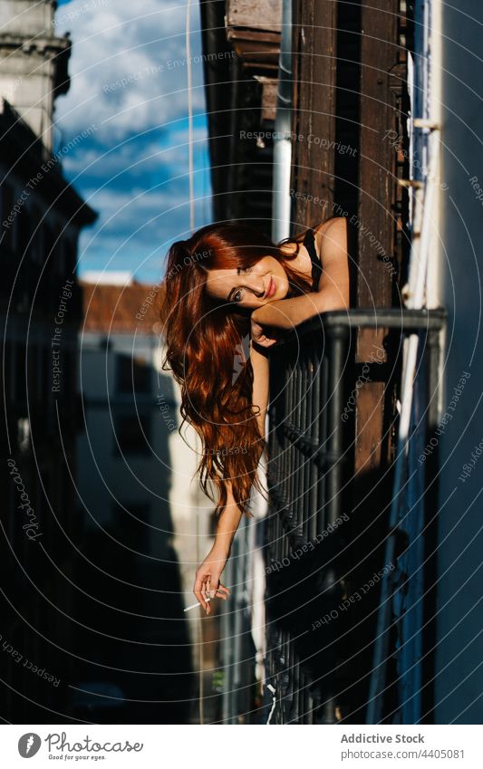 Smiling woman with cigarette sticking out of balcony stick out redhead smile chill sunset smoker enjoy female lean railing cheerful city residential building