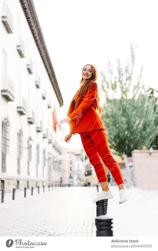 Stylish woman standing on parking bollard in city style orange suit trendy street vivid female color bright balance fashion urban red hair redhead ginger lady