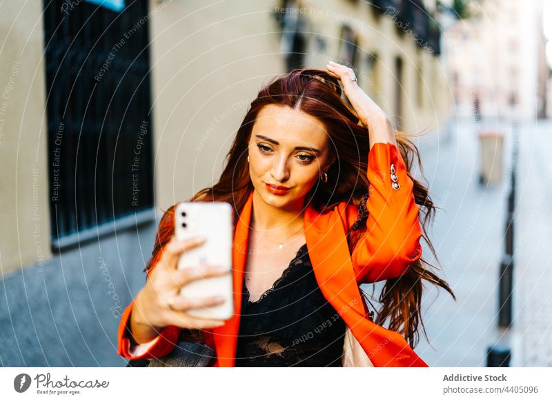 Trendy redhead woman taking selfie in city smartphone ginger self portrait orange vivid color female street style urban fashion memory modern device gadget