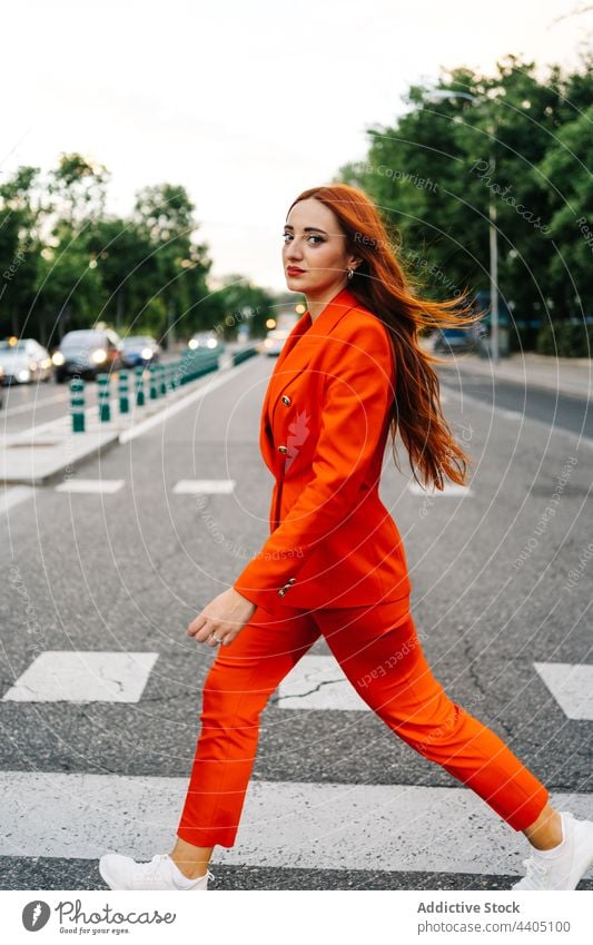Trendy redhead woman crossing road in city crosswalk suit orange vivid style ginger female fashion confident trendy long hair contemporary outfit appearance