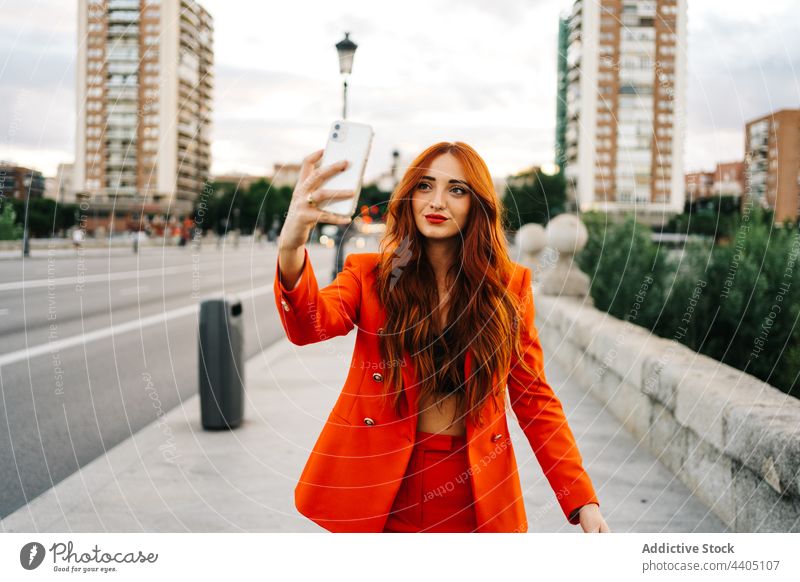 Smiling woman with ginger hair taking selfie in street city smartphone self portrait red hair orange suit trendy female cheerful style smile urban positive