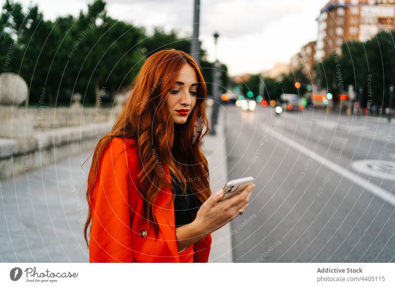 Redhead woman browsing on smartphone in city social media orange suit vibrant female mobile gadget device red hair redhead ginger using communicate internet