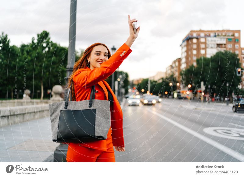 Cheerful woman with red hair catching taxi in city redhead wave hand gesture cab outstretch arm raised female street hail cheerful smile happy road car positive