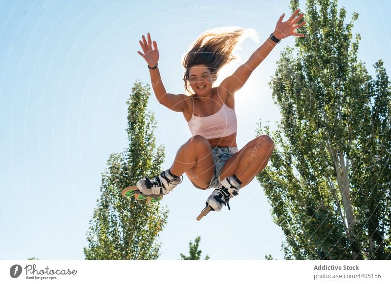 Energetic woman jumping in rollerblades in park trick stunt active summer energy moment female activity motion dynamic sunlight freedom skater sunny blue sky