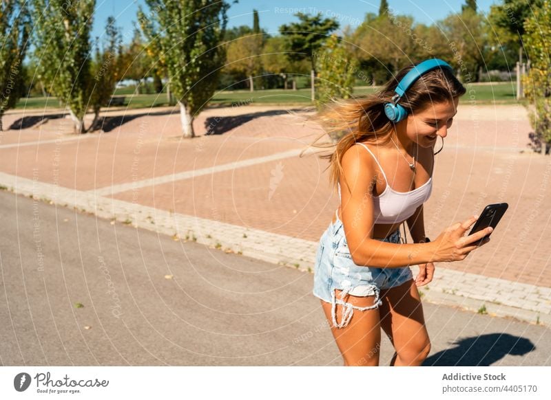 Cheerful woman rollerblading and using smartphone rollerblade listen music city summer skater ride female device gadget cheerful happy internet headphones