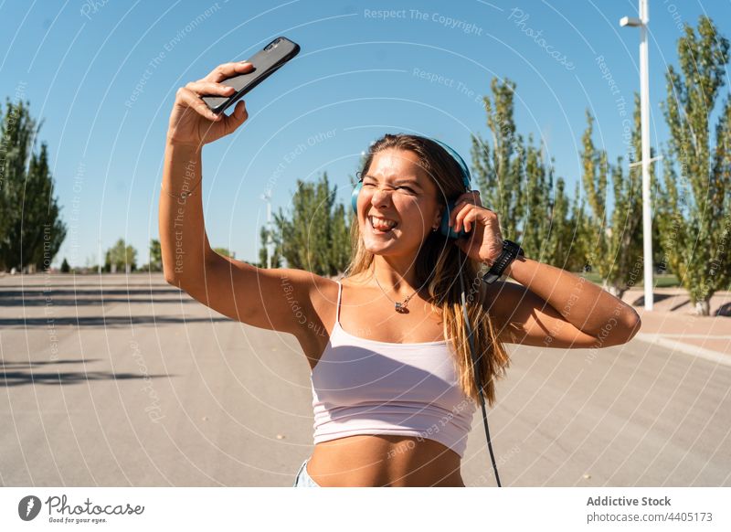 Smiling woman in rollerblades taking selfie in street smartphone city summer self portrait moment skater female happy cheerful music memory sticking tongue out