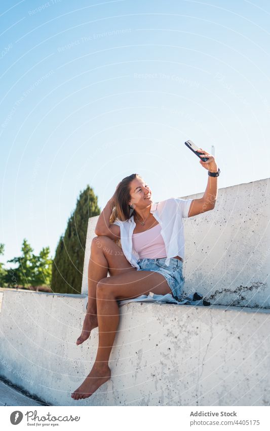 Smiling woman taking selfie in street smartphone city summer self portrait moment female happy cheerful memory mobile device smile cellphone take photo using
