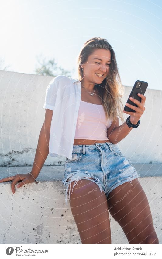 Smiling woman browsing smartphone in street city summer moment female happy cheerful text message mobile device smile cellphone using gadget urban enjoy