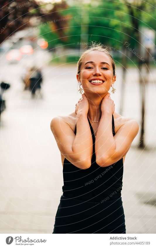Cheerful trendy woman smiling and standing in street style city smile touch neck cheerful outfit urban female positive charming appearance individuality happy