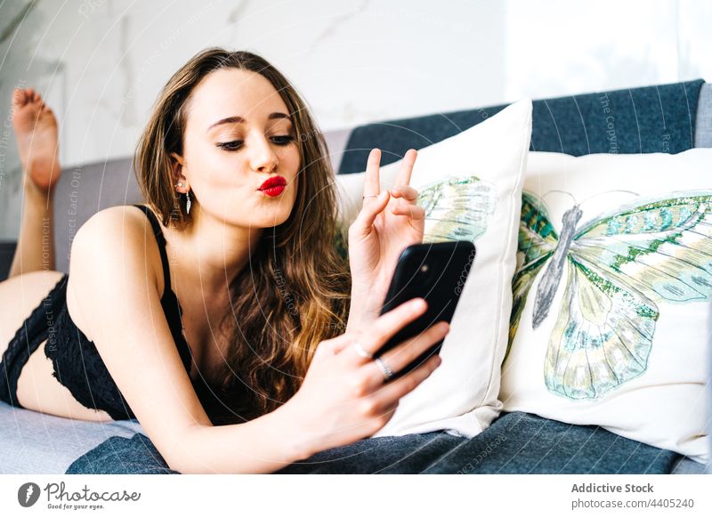 Cheerful woman in lingerie browsing smartphone in living room underwear using message cheerful sofa female home mobile social media lying slim slender content