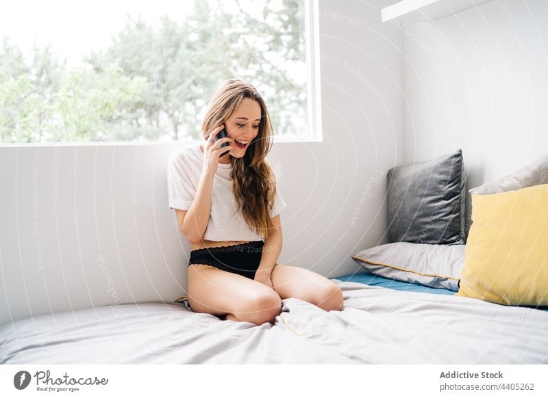 Cheerful woman talking on smartphone on bed domestic panties speak conversation mobile female call young communicate cheerful positive happy cellphone gadget
