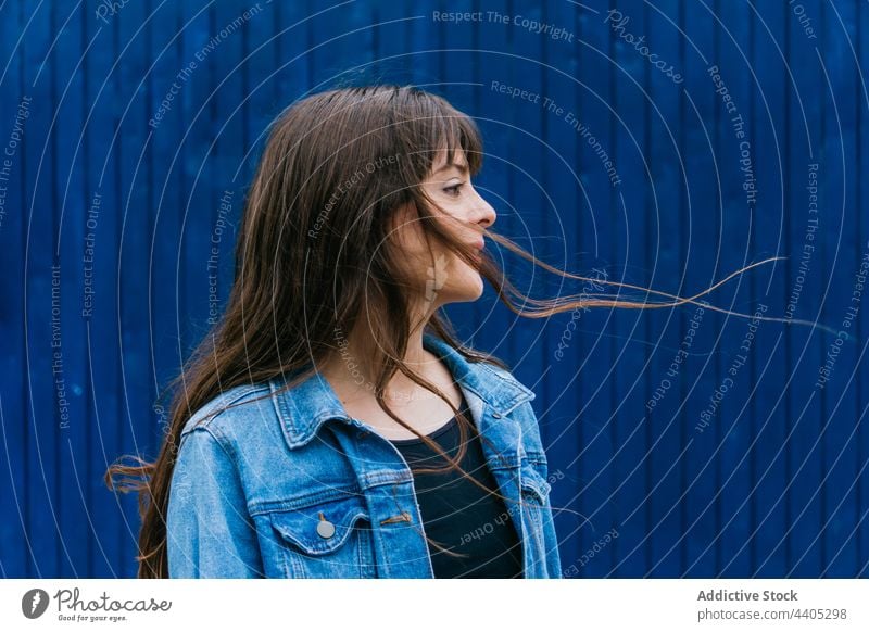 Serene woman with flying hair on blue background long hair serene color style brown hair tranquil city female urban peaceful outfit brunette modern trendy calm