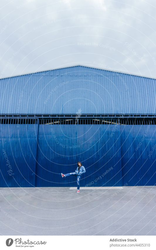 Woman jumping along blue building in city woman walk street wall smile cheerful color denim happy stroll urban female style cloth trendy modern facade outfit