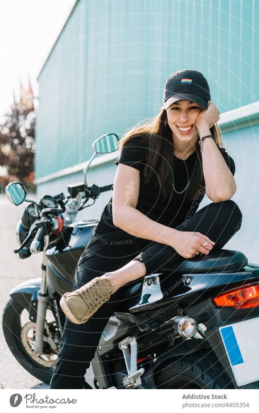 Cheerful woman sitting on motorbike and looking at camera motorcycle biker motorcyclist cheerful parked city smile rider female transport vehicle urban street