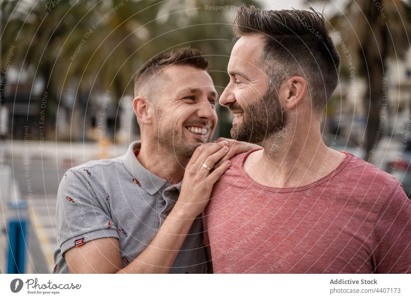 Cheerful gays embracing while looking away in harbor couple same sex embrace love speak relationship spend time sincere men town homosexual smile romantic