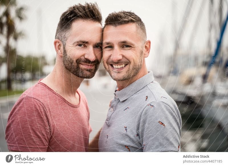 Cheerful gays embracing while looking at camera on urban road couple same sex embrace love speak relationship spend time sincere men town homosexual smile