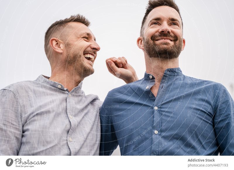 Cheerful couple of gays talking under light sky lgbt laugh interact spend time relationship romantic candid men same sex contemplate sincere content glad