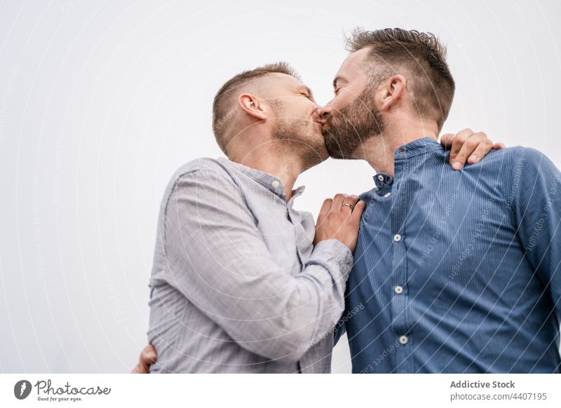 Cheerful couple of gays kissing under light sky lgbt laugh interact spend time relationship romantic candid men same sex contemplate talk sincere content glad