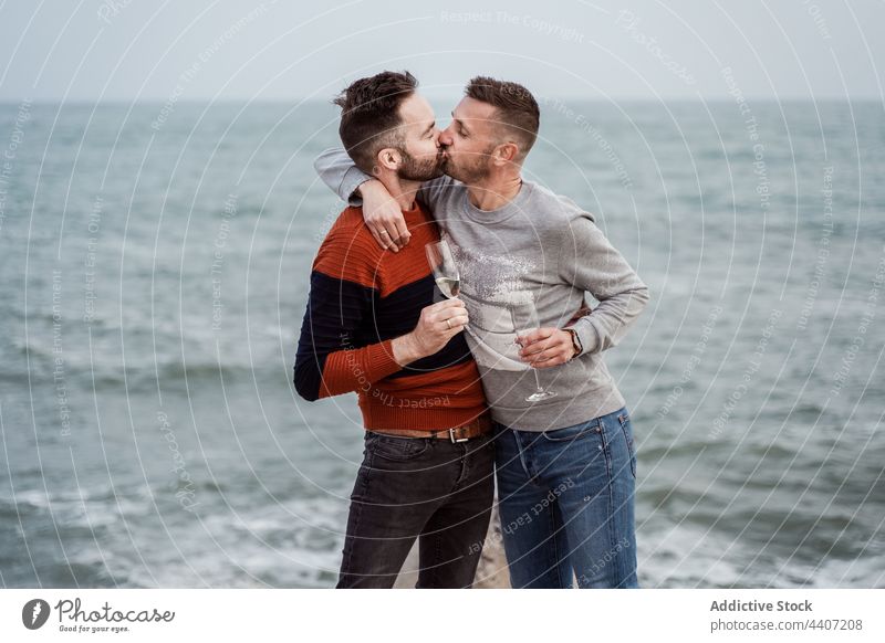 Couple of gays kissing on sea shore champagne beverage alcohol enjoy relationship romance glass seashore men couple lgbt spend time romantic drink ocean coast