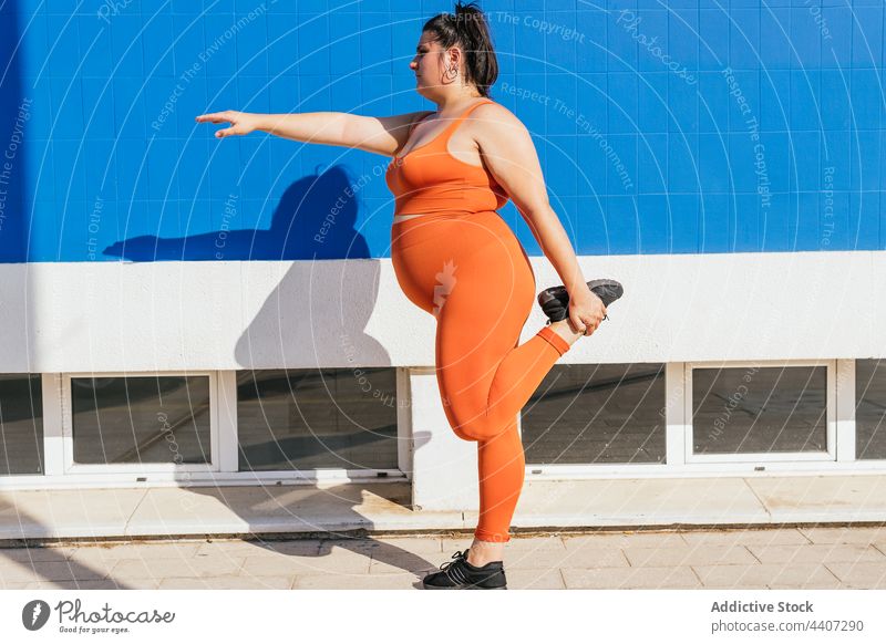 Sportswoman with curvy body stretching leg on urban pavement athlete sport leg raised workout training exercise plump healthy lifestyle vitality wellness street