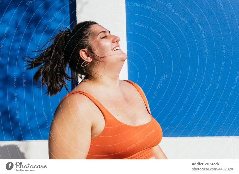 Smiling overweight ethnic athlete with closed eyes on street cheerful flying hair having fun sport eyes closed wellbeing plump woman sportswoman plus size