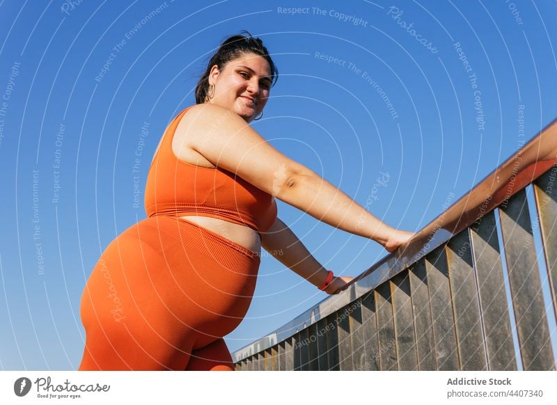 Ethnic sportswoman with excess weight leaning on the fence in sunlight blue sky contemplative body break admire overweight pleasant alone athlete plump