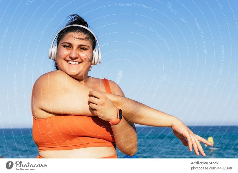 Smiling overweight ethnic sportswoman in headset under a blue sky athlete headphones listen music free time smile wall using gadget device cellphone wireless