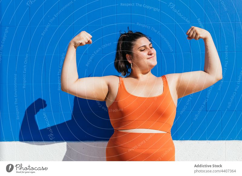 Strong overweight ethnic sportswoman showing biceps in sunlight strong power confident workout training plus size street self assured gesture strength muscle