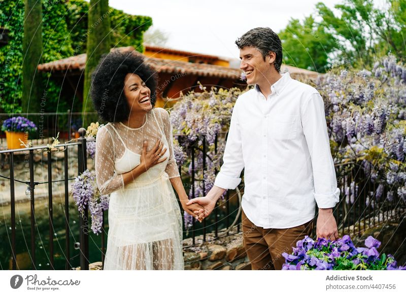 Positive multiethnic couple holding hands in park with flowers garden walk bloom cheerful together relationship multiracial diverse black african american enjoy