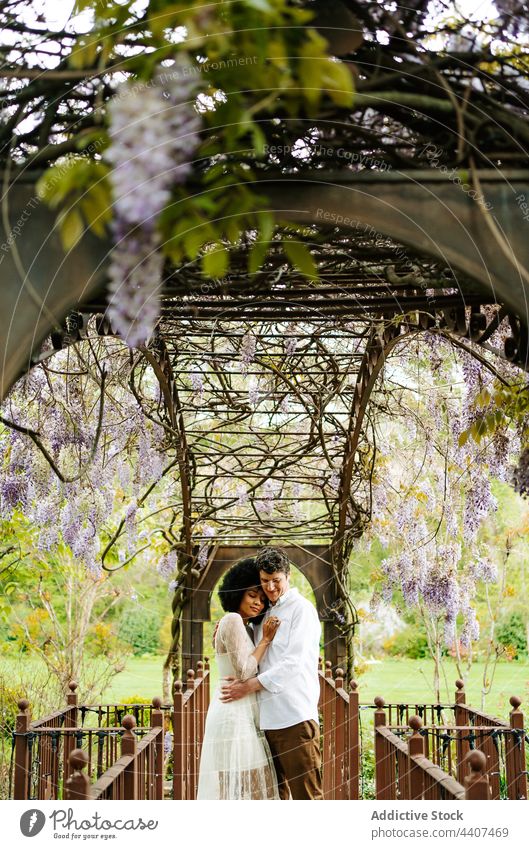 Delicate multiethnic couple hugging under natural arch of flowers love garden embrace tender gentle bloom multiracial diverse black african american eyes closed