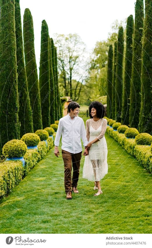 Content multiethnic couple walking along alley in park holding hands relationship love together garden smile multiracial diverse black african american stroll