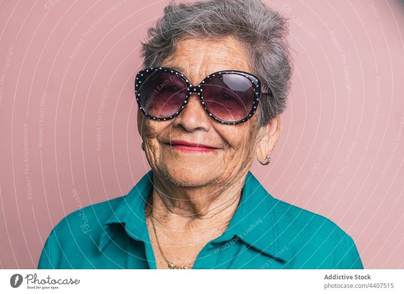 Stylish elderly woman in sunglasses in studio aged style trendy modern senior smile fashion cheerful female happy contemporary positive outfit glad gray hair