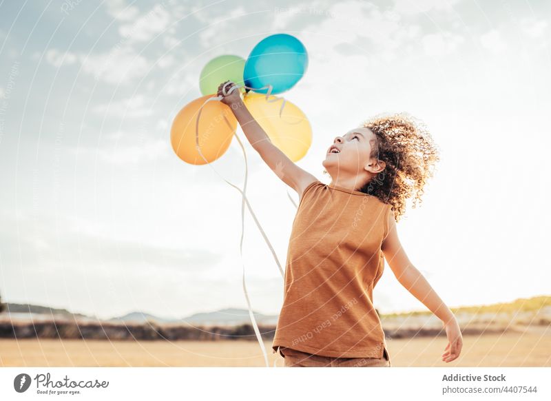 Carefree ethnic child playing with colorful balloons in field air balloon wind playful carefree freedom summer kid smile cheerful childhood happy cute fly