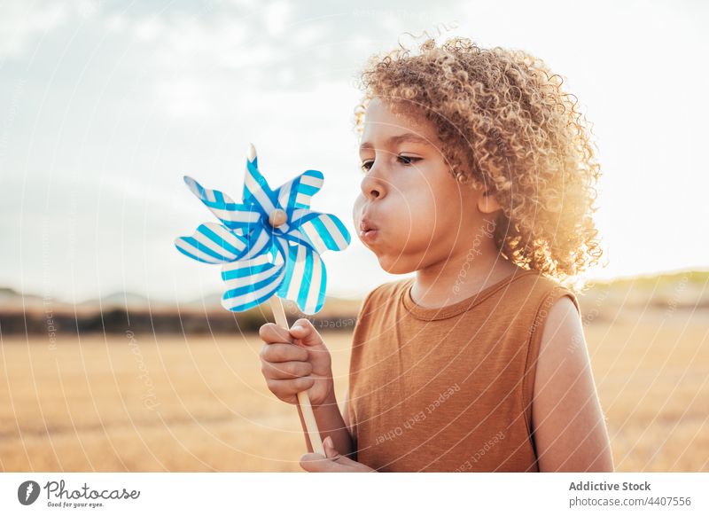 Ethnic child playing with toy windmill in field pinwheel blow summer entertain having fun playful ethnic kid childhood cute curly hair afro hairstyle carefree