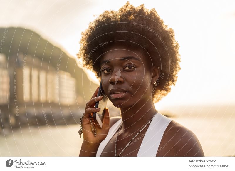Black woman talking on smartphone near sea in sunset speak embankment using cellphone summer female black african american ethnic stand communicate call