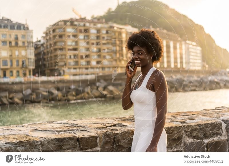 Cheerful black woman talking on smartphone near sea in sunset speak embankment using cellphone summer female african american ethnic stand communicate call