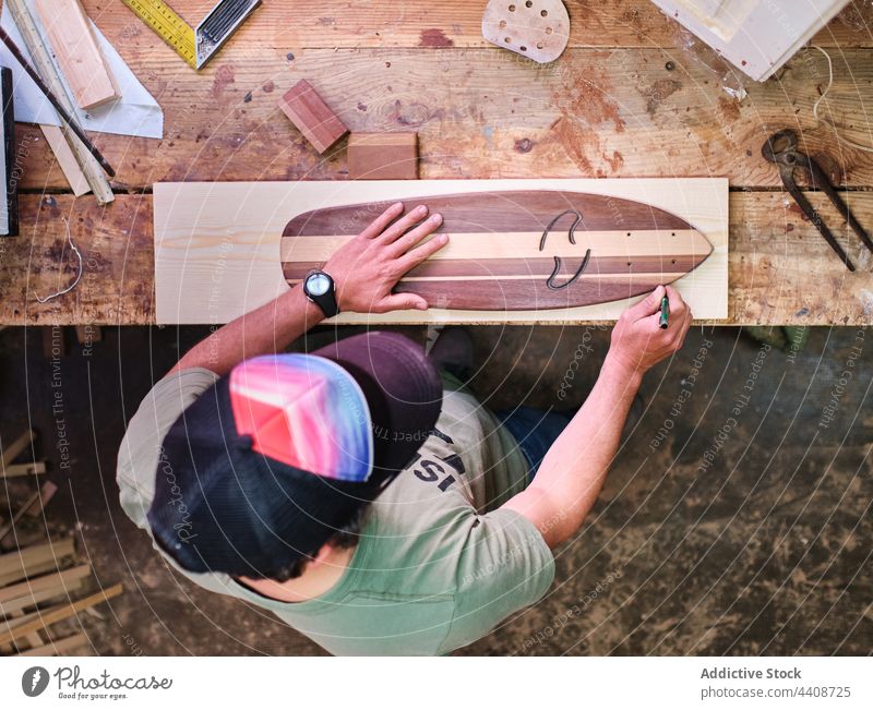 Anonymous craftsman with marker and wooden blocks on workbench trace skateboard manufacture plank woodwork accuracy cheerful handmade small business joiner