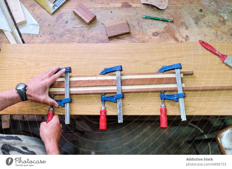 Crop craftsman clamping wooden sticks in workshop carpenter woodwork glue assemble professional precise instrument workbench woodworker plank job artisan tool