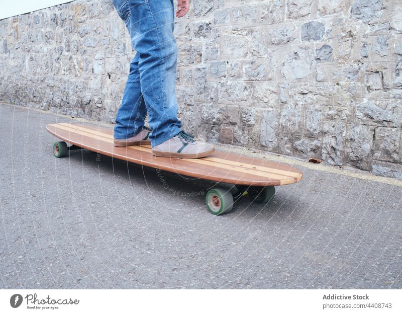 Crop skater riding handmade longboard on road ride active sport spare time weekend stone wall practice freedom jeans street skateboarder modern style creative