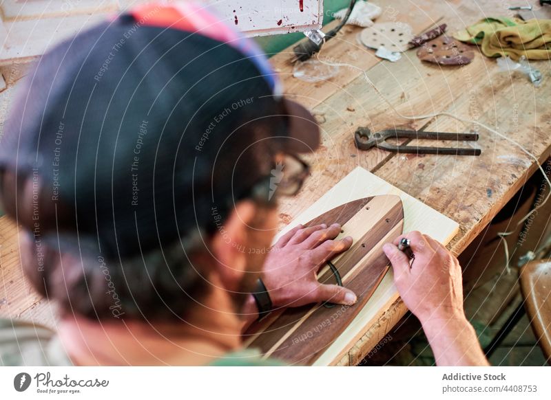 Anonymous craftsman with marker and wooden blocks on workbench trace skateboard manufacture plank woodwork accuracy cheerful handmade cap small business joiner