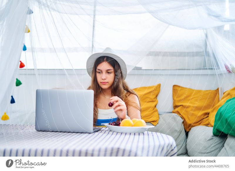 Woman eating berries and browsing laptop woman cherry berry surfing using backyard tent female netbook summer internet fresh enjoy weekend device gadget online