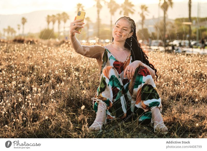Delighted woman with vitiligo taking a self portrait with the smartphone on meadow selfie browsing field summer sunset skin condition using female positive
