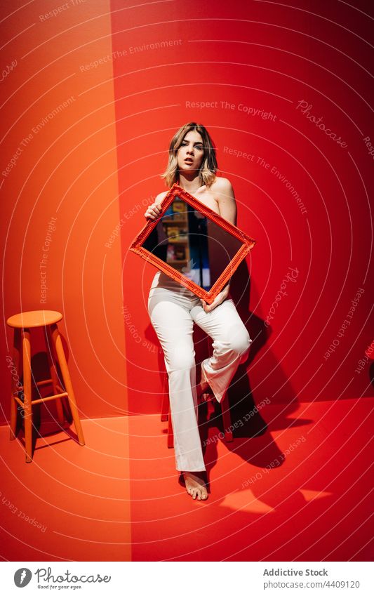 Stylish model with mirror resting on stool reflection style sensual barefoot millennial woman portrait light charming pants sit colorful frame rectangular shape