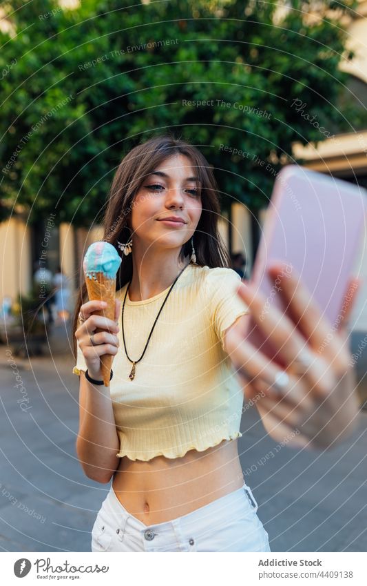 Smiling woman with ice cream taking selfie on smartphone dessert treat moment spare time street using gadget device self portrait memory satisfied cone smile