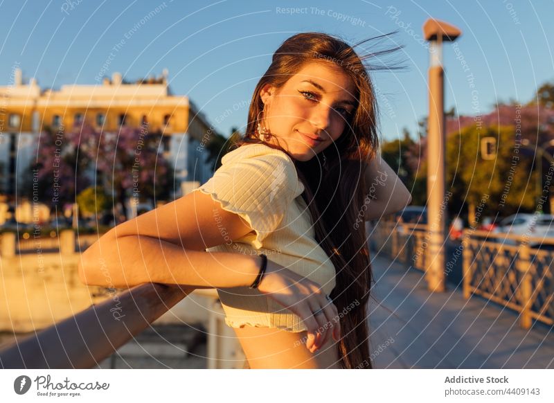 Charming woman touching neck on urban bridge in twilight touch neck flying hair gentle sincere charming pleasant evening portrait kind friendly city windy