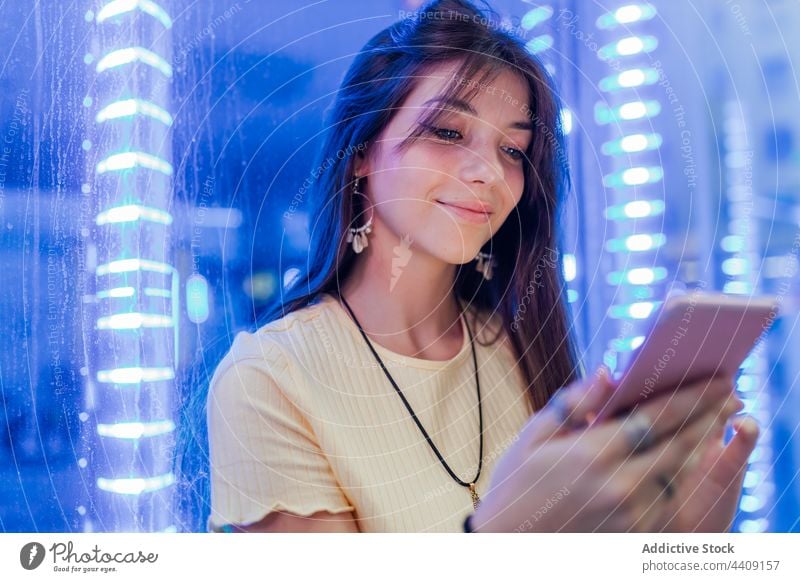 Smiling woman chatting on smartphone in neon lights interested internet online spare time town using gadget device watching cellphone gentle sincere charming