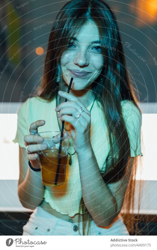 Cheerful woman with glass of beverage at night drink refreshment content sincere friendly dusk portrait style straw transparent charming kind enjoy pleasant