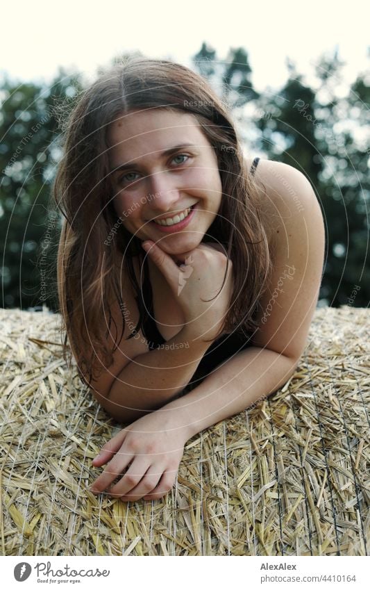 Young dimpled woman smiles and looks at the camera while lying on a bale of straw Brunette Athletic 18 - 30 years Adults Long-haired Esthetic